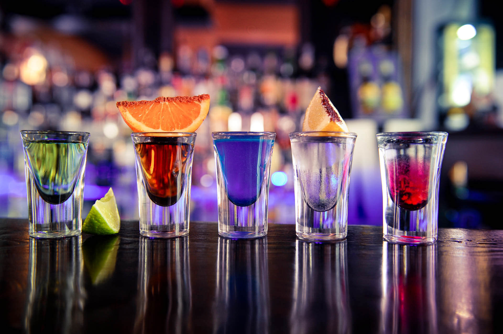 Five shot glasses with colourful alcohol on bar